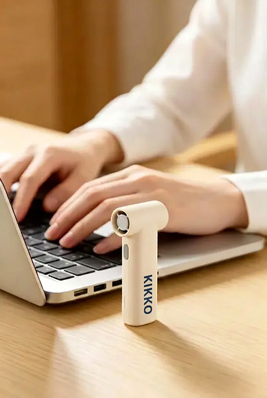 Stands upright on your desk for hands-free cooling while you work. KIKKO Portable Fan standing upright on a work desk beside a laptop for personal cooling at the office